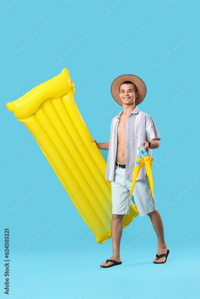 Teenage boy with inflatable mattress and flippers on blue background