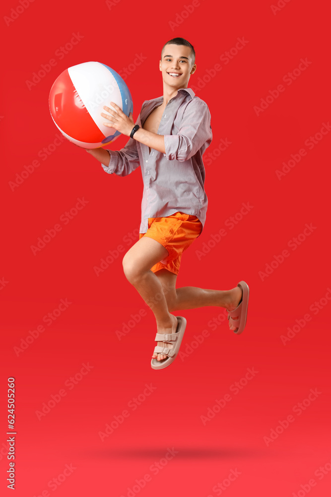 Teenage boy with beach ball jumping on red background