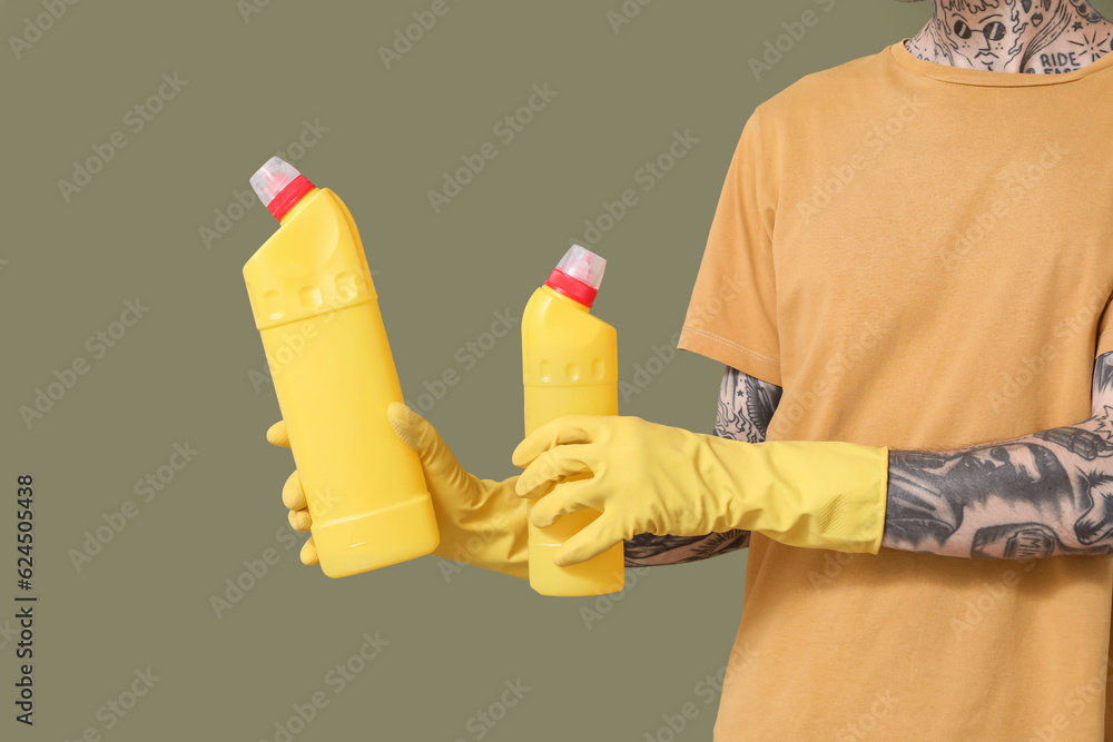 Young tattooed man with bottles of detergent on green background, closeup