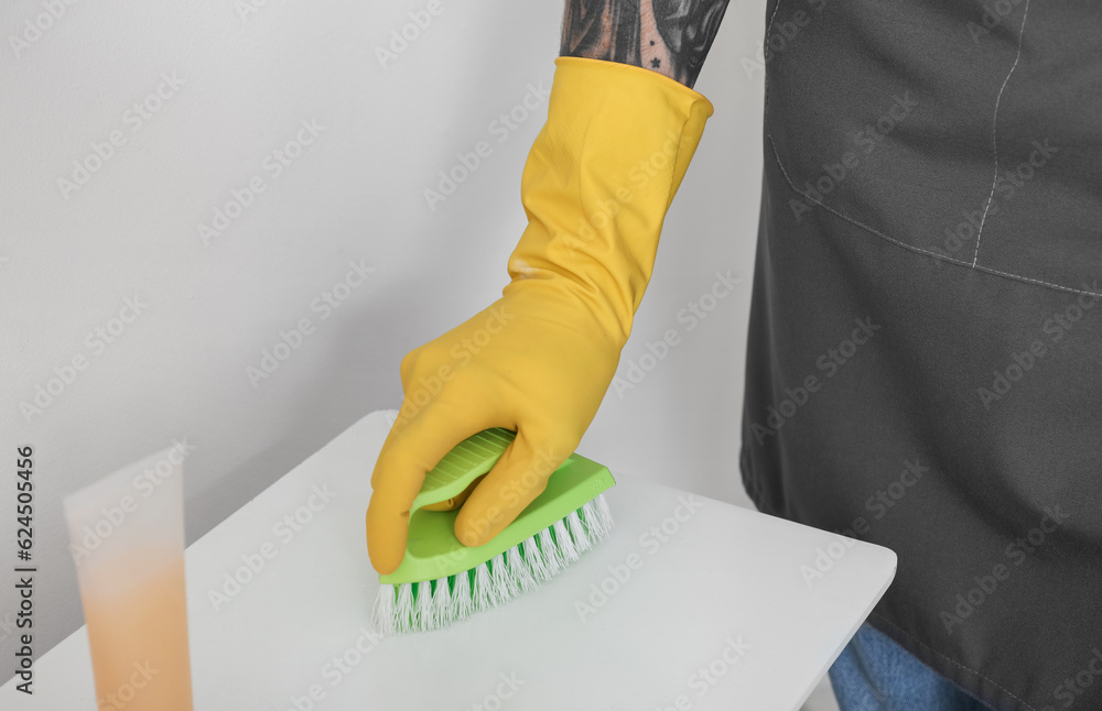 Young tattooed man cleaning shelf with brush in bathroom, closeup