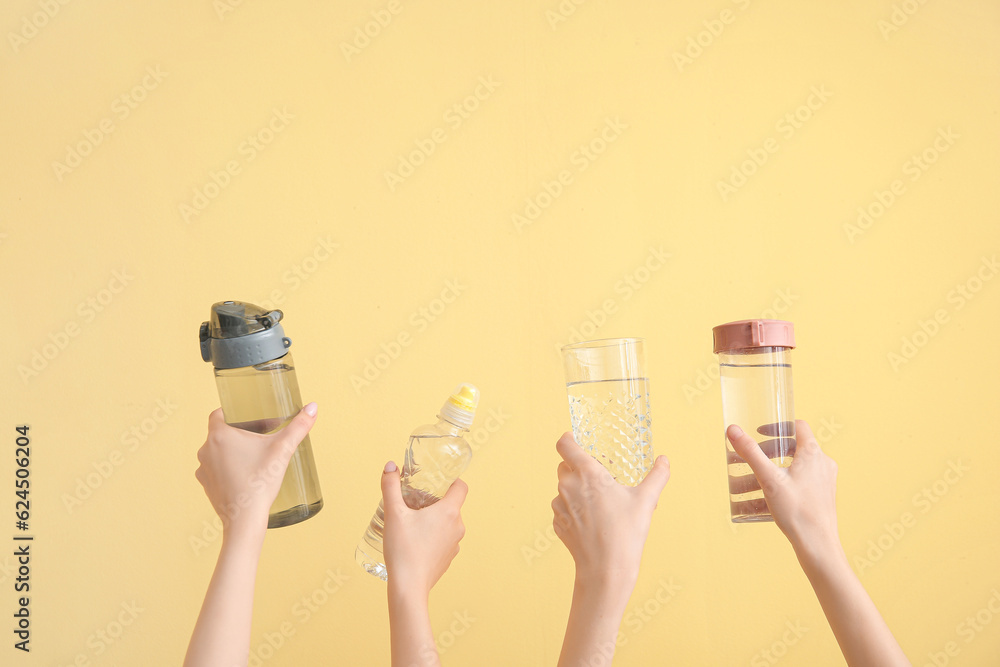 Women holding sports bottles and glass with clean water on yellow background