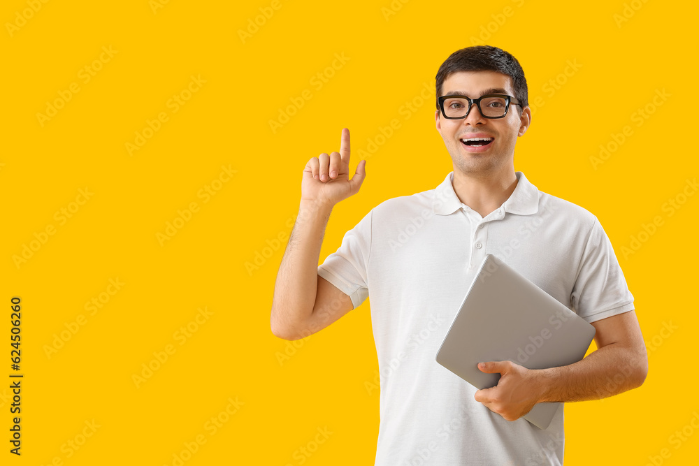 Male programmer with laptop pointing at something on yellow background