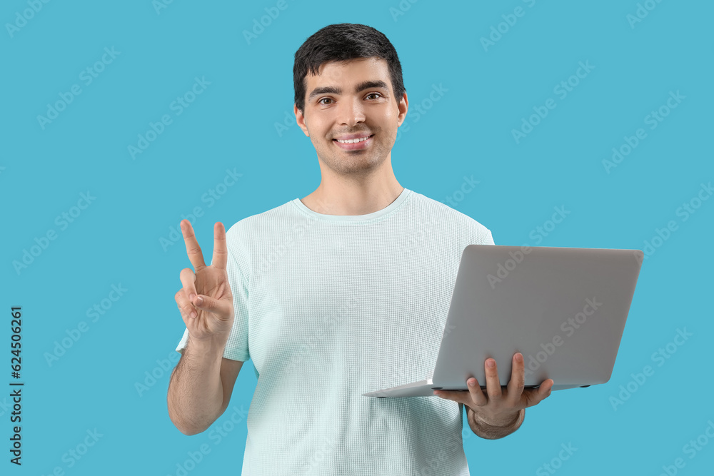 Male programmer with laptop showing victory gesture on blue background