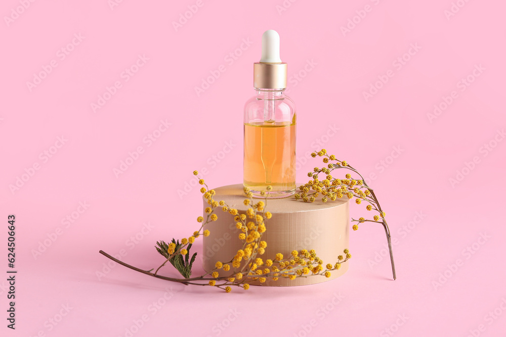 Podium with bottle of essential oil and mimosa flowers on pink background