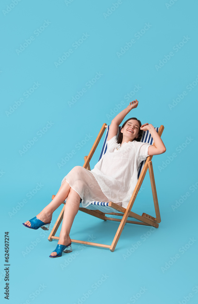 Young woman relaxing in deck chair on blue background