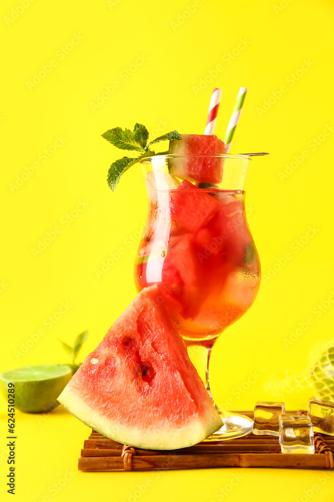 Glass of fresh watermelon lemonade with lime and mint on yellow background