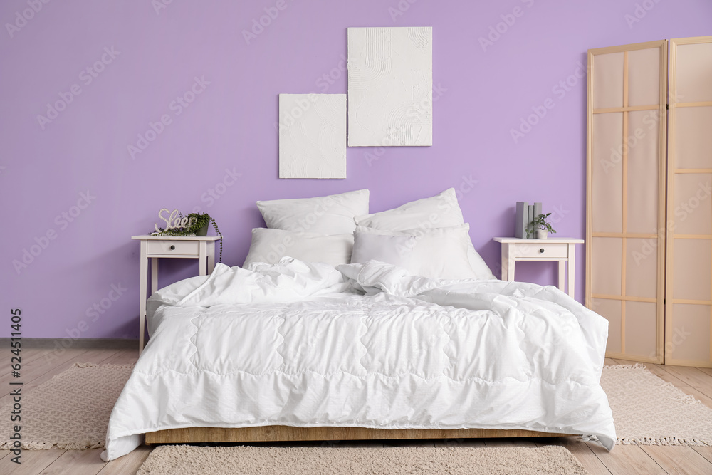 Interior of stylish bedroom with comfortable bed, white pillows, bedside tables and folding screen