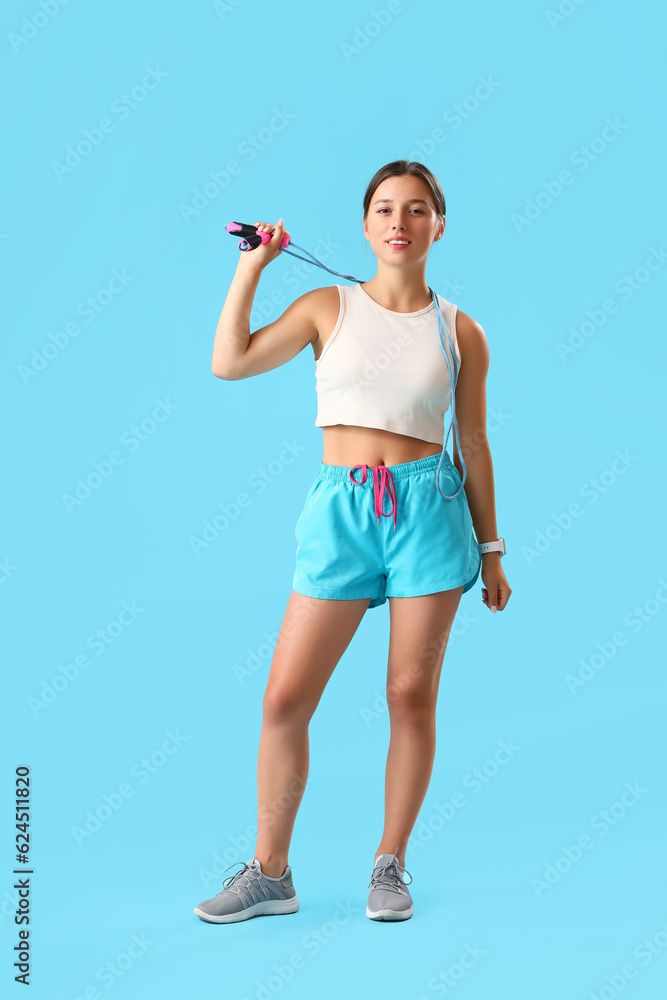 Sporty young woman with jumping rope on blue background