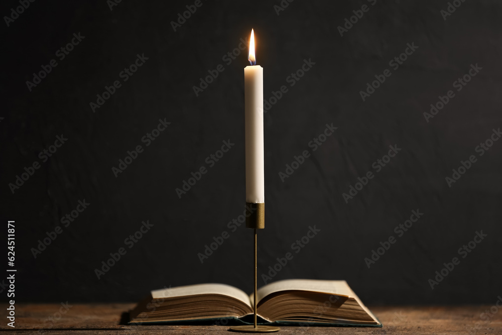 Beautiful burning candle and book on black background