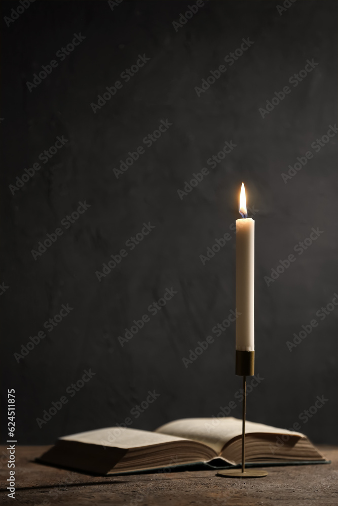 Beautiful burning candle and book on black background