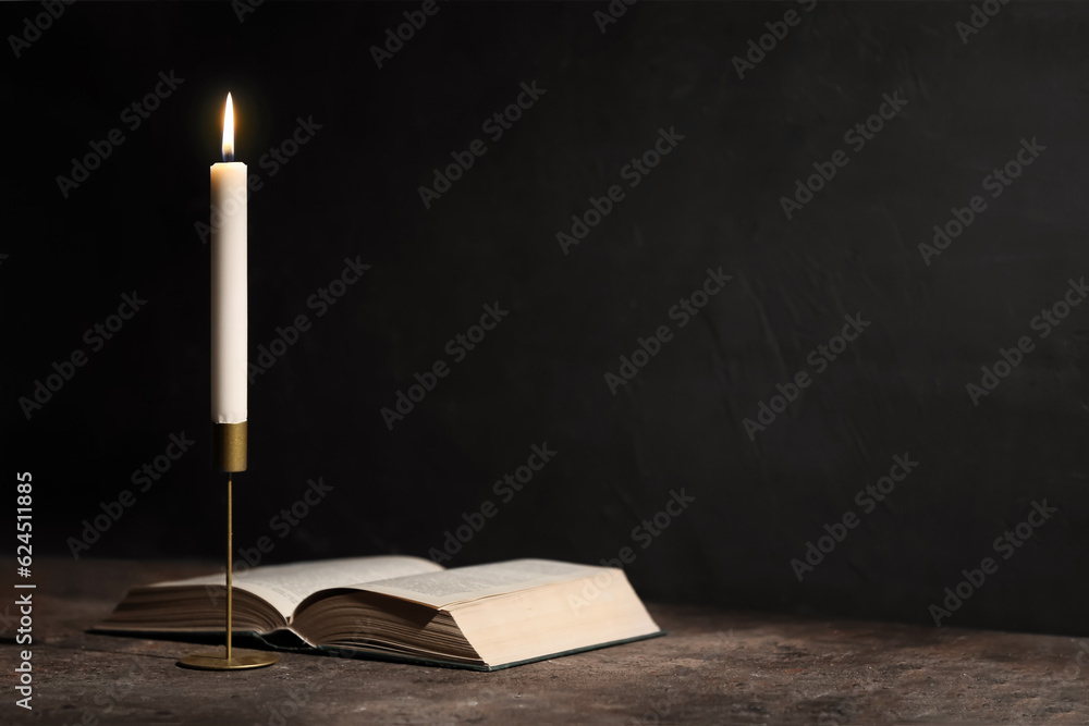 Beautiful burning candle and book on black background