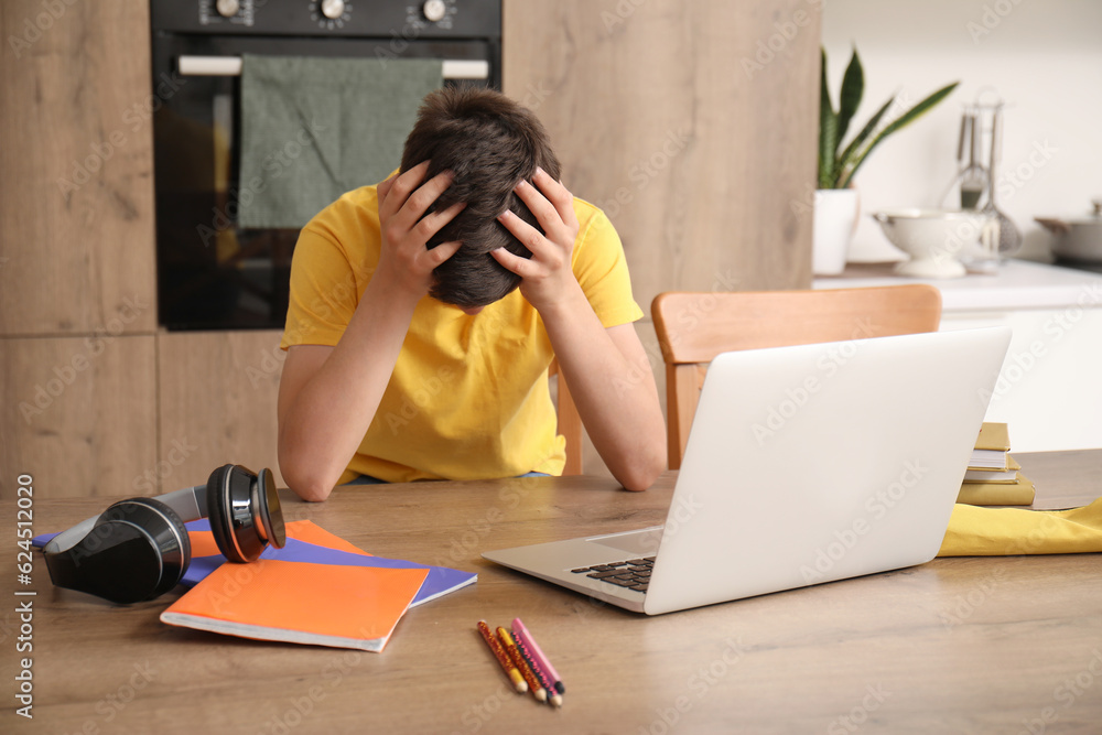 Stressed little boy studying online with laptop in kitchen