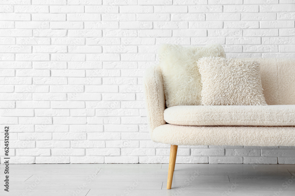 Cozy white sofa with pillows near brick wall