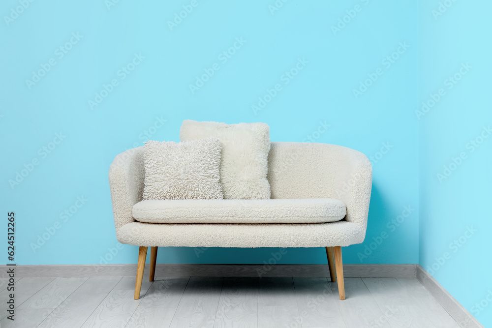 Cozy white sofa with pillows near blue wall