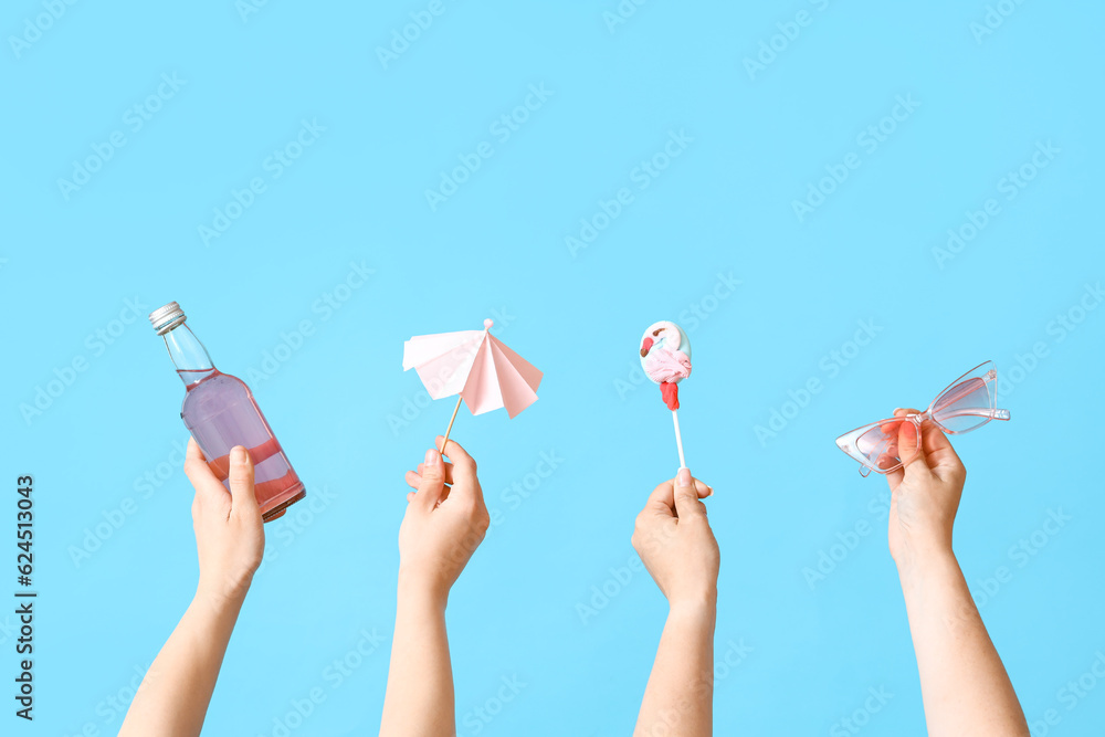 Female hands with bottle of cocktail and sunglasses on blue background