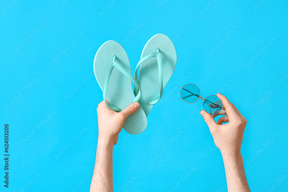 Male hands with flip flops and sunglasses on blue background