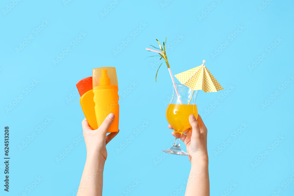 Female hands with cocktail and bottles of sunscreen cream on blue background