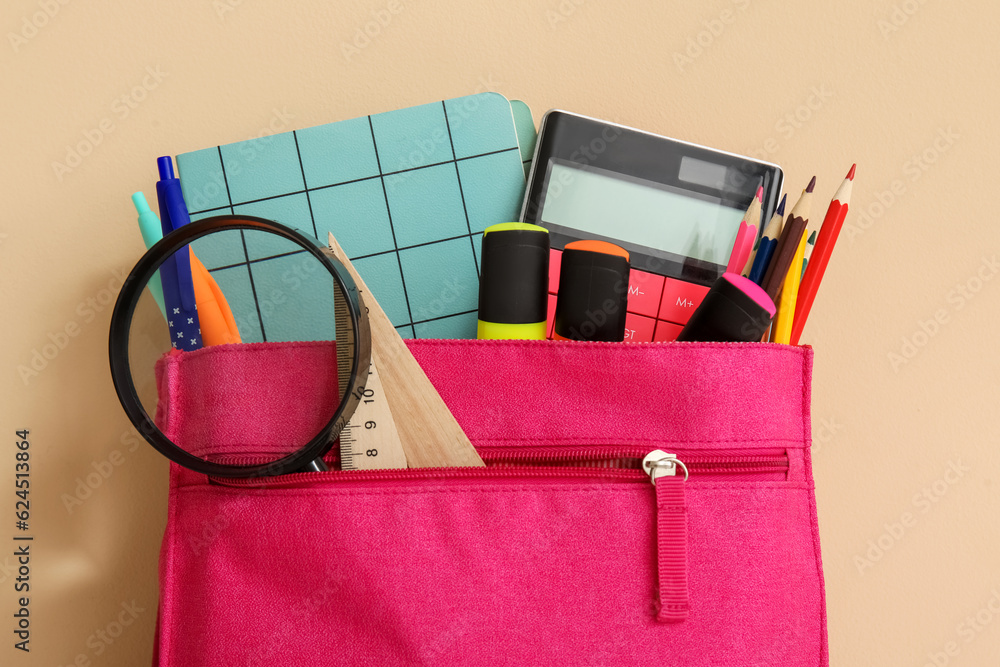 Pink school backpack with different stationery and magnifier on orange background