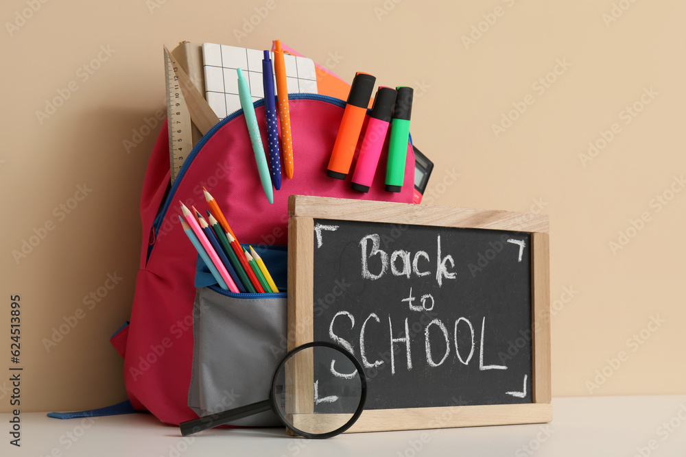 School backpack, different stationery and blackboard with text BACK TO SCHOOL on white table near or