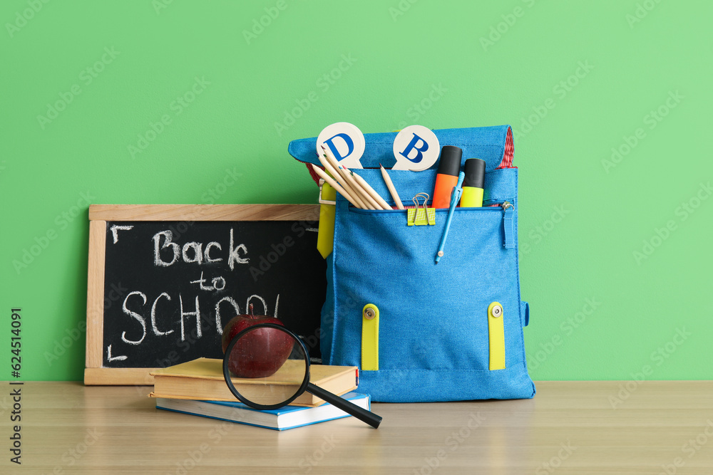 School backpack, different stationery and blackboard with text BACK TO SCHOOL on wooden table near g