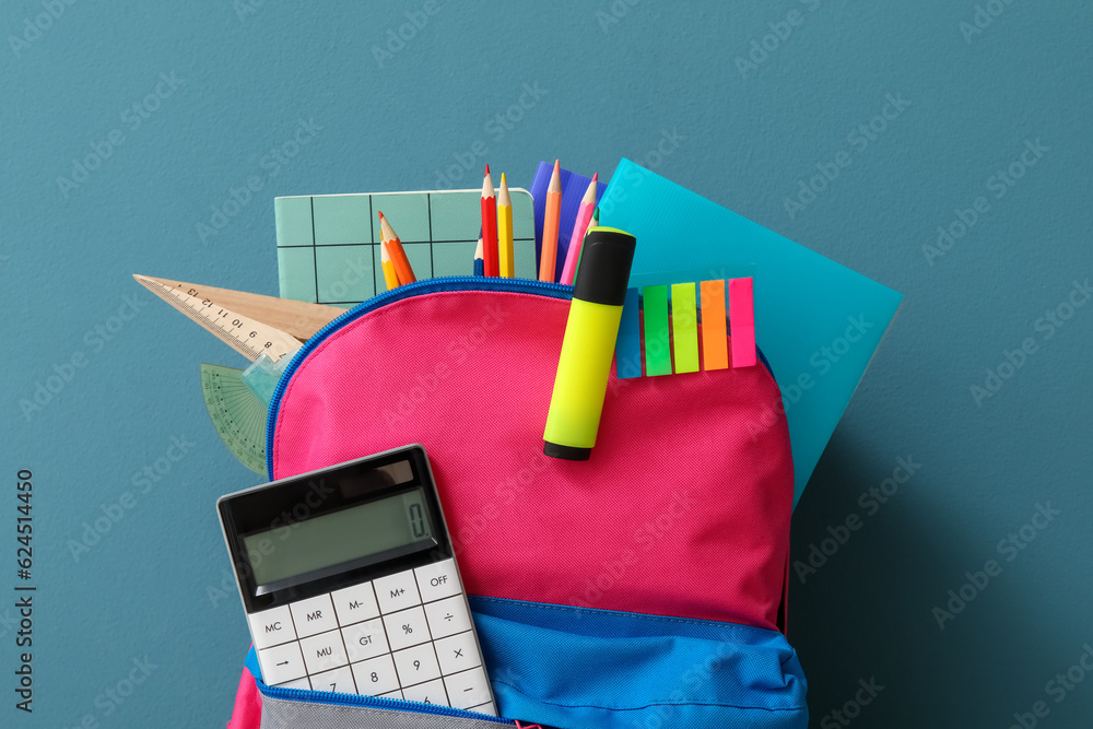 Colorful school backpack with different stationery and calculator on blue background