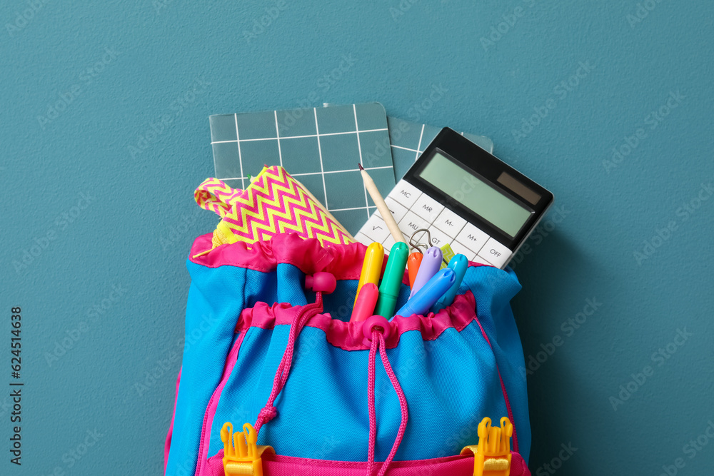 Colorful backpack with different stationery and calculator on blue background