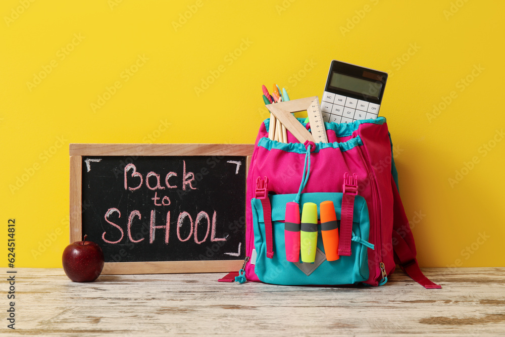 Colorful school backpack, stationery and blackboard with text BACK TO SCHOOL on wooden table near ye