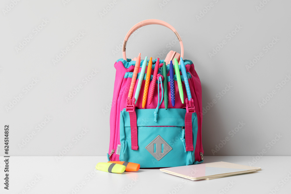 Colorful school backpack with different stationery on white table near wall