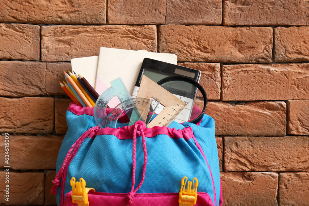 Colorful school backpack with different stationery on brown brick background