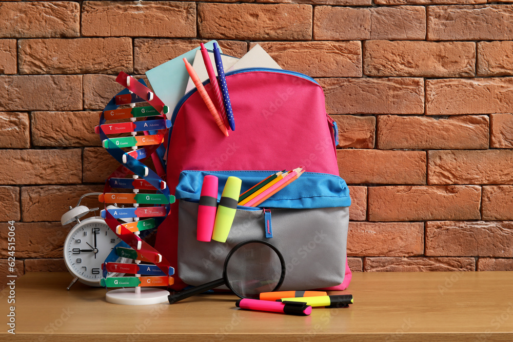 Colorful school backpack with different stationery and molecular model on wooden table near brown br