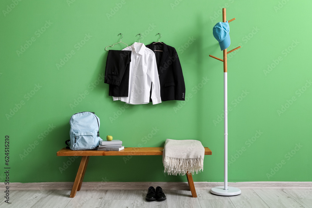 Rack with cap, bench, backpack, shoes and stylish school uniform hanging on green wall in room