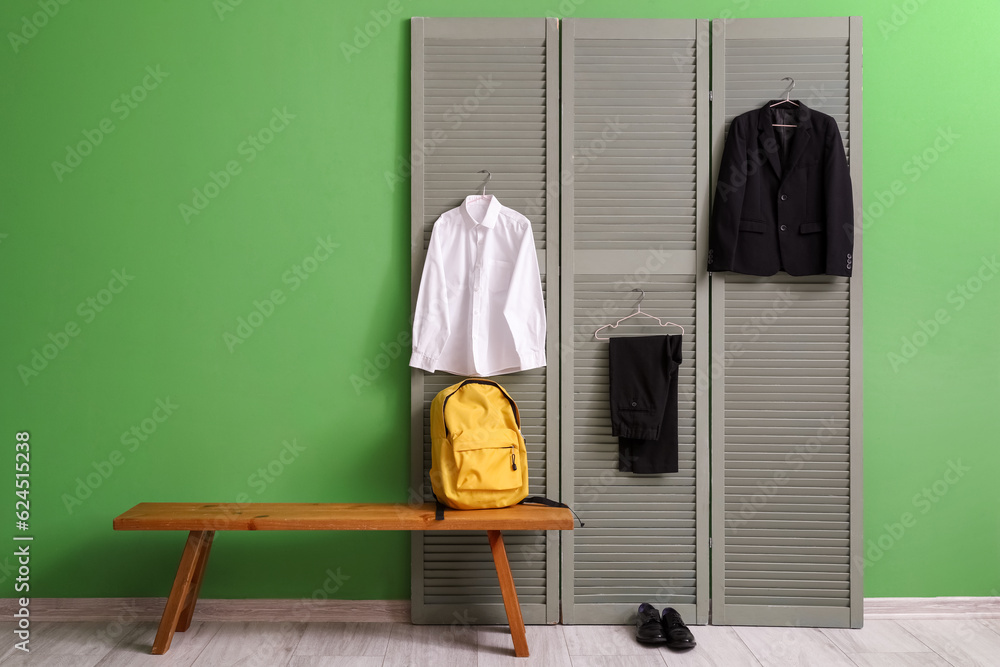 Bench with backpack, shoes and stylish school uniform hanging on folding screen in room