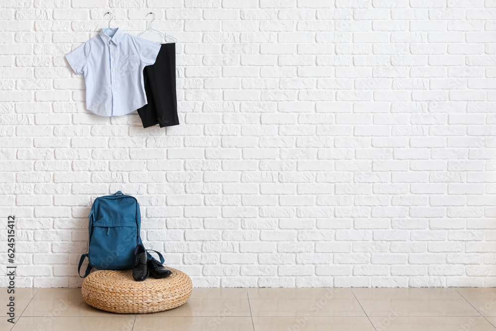 Pouf with backpack, shoes and stylish school uniform hanging on light brick wall in room