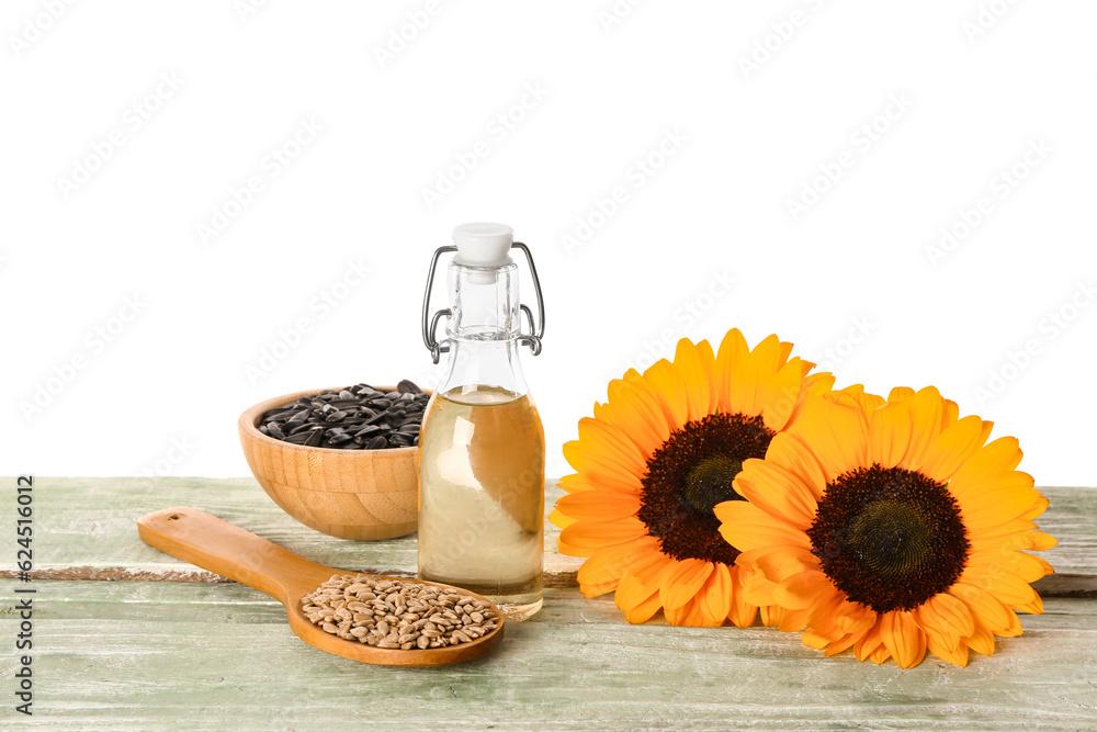 Sunflowers, seeds and bottle of oil on table against white background