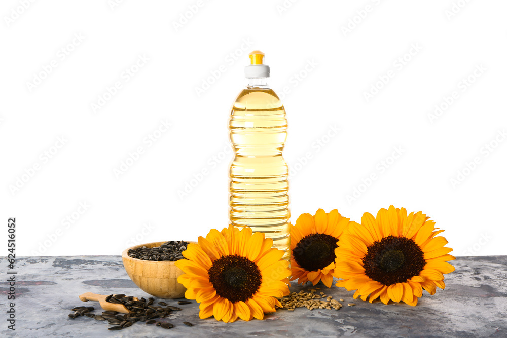 Sunflowers, seeds and bottle of oil on table against white background