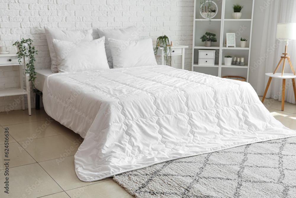 Cozy bed with white blanket and pillows in interior of light bedroom