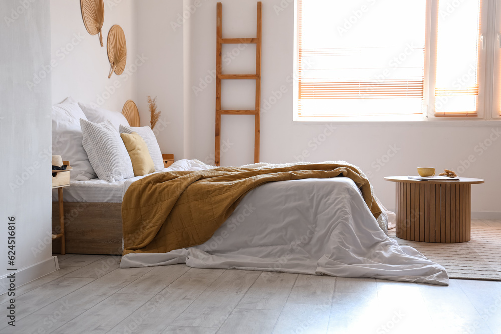 Cozy bed with white blanket and coffee table in interior of light bedroom