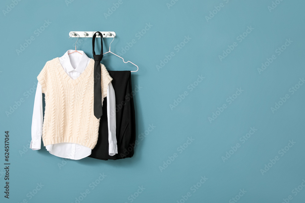 Stylish school uniform hanging on color wall