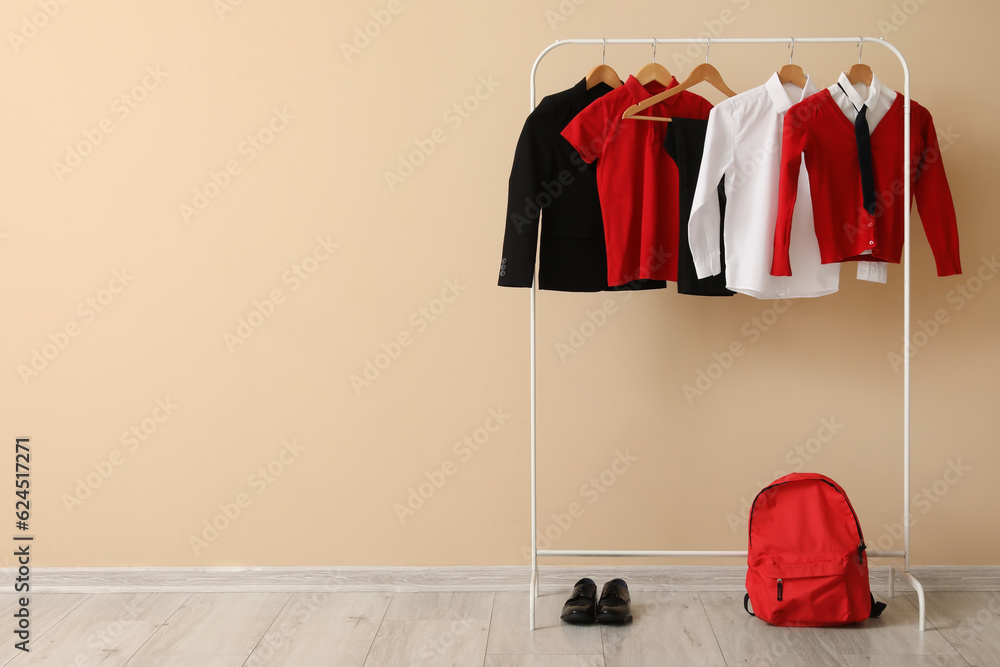 Rack with stylish school uniform, backpack and shoes near color wall