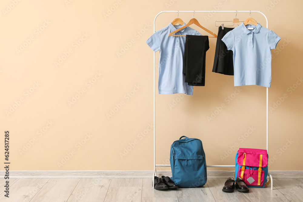 Rack with stylish school uniform, backpacks and shoes near color wall