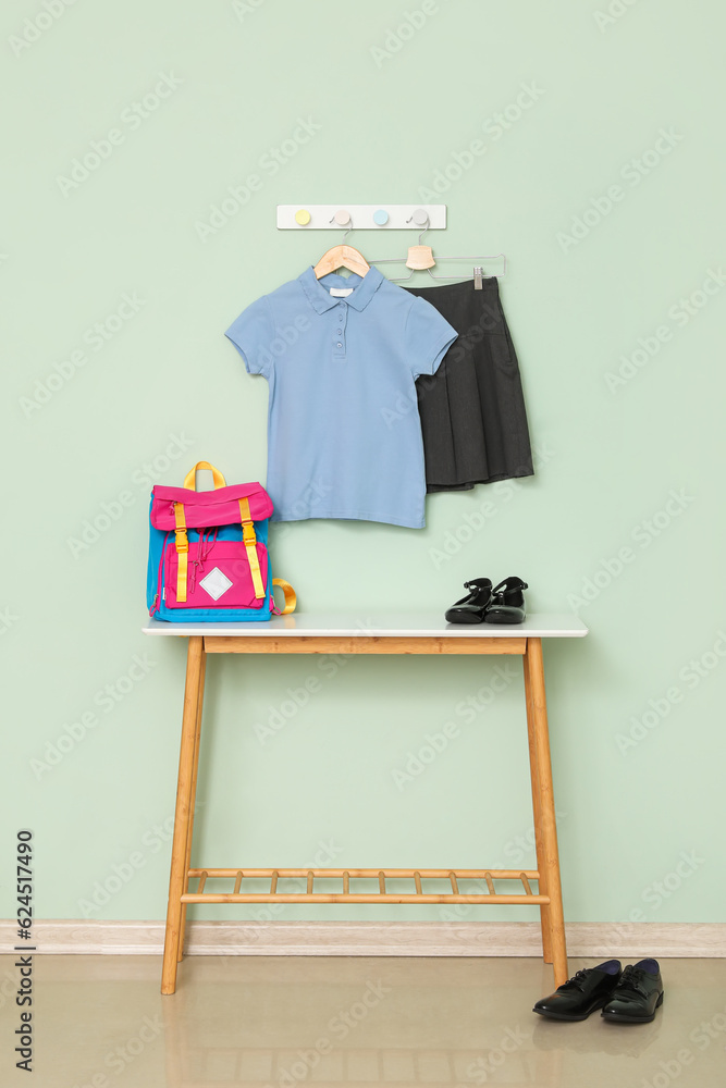 Table with school backpack, shoes and uniform hanging on color wall