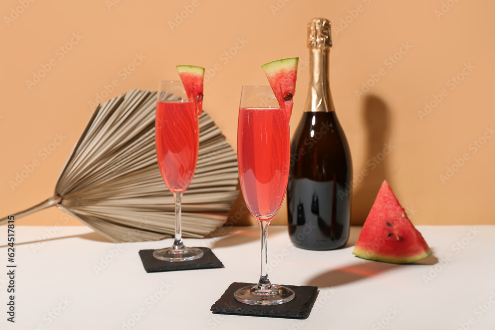 Glasses of tasty watermelon cocktail with champagne bottle on white table near orange wall