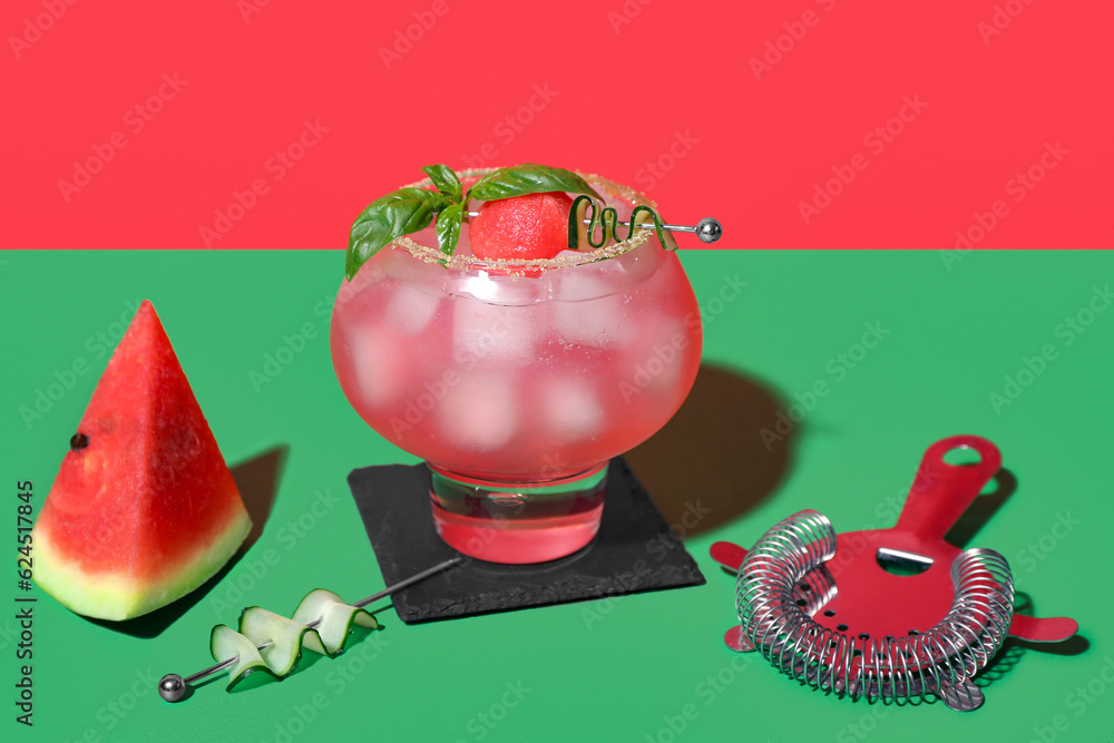 Glass of tasty watermelon cocktail with strainer on green table near red wall