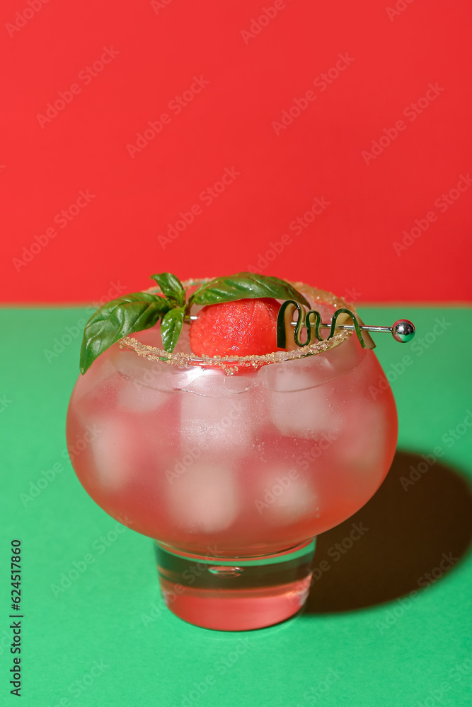 Glass of tasty watermelon cocktail on green table near red wall