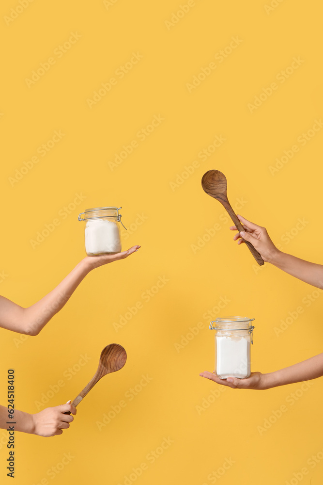 Female hands with jars and wooden spoons on yellow background