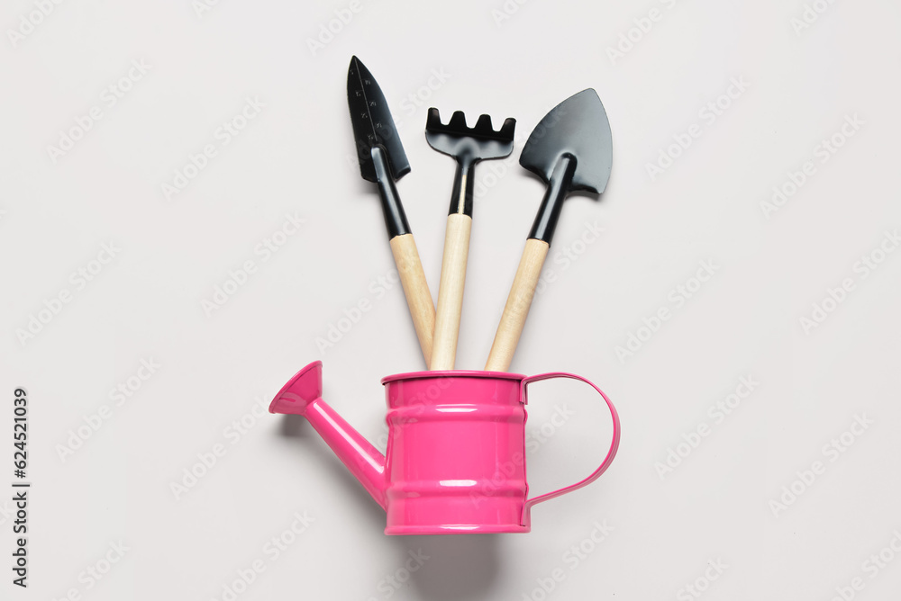 Watering can with gardening rake and shovels on white background