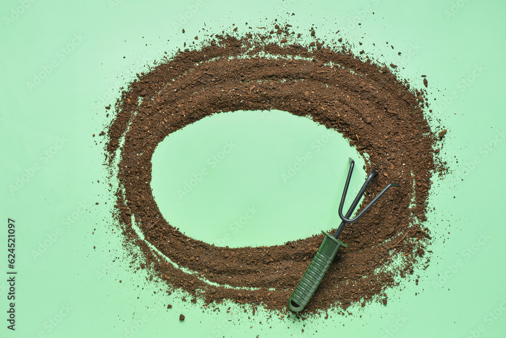 Frame made of soil with gardening rake on green background