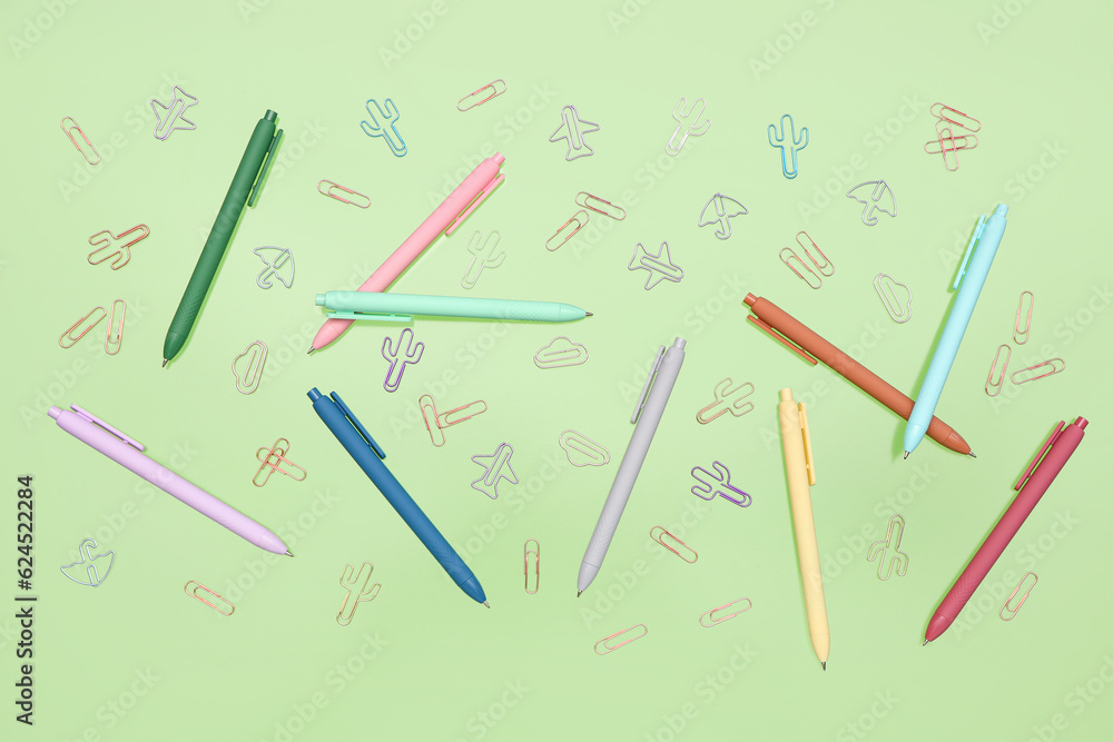 Colorful pencils and paperclips on green background