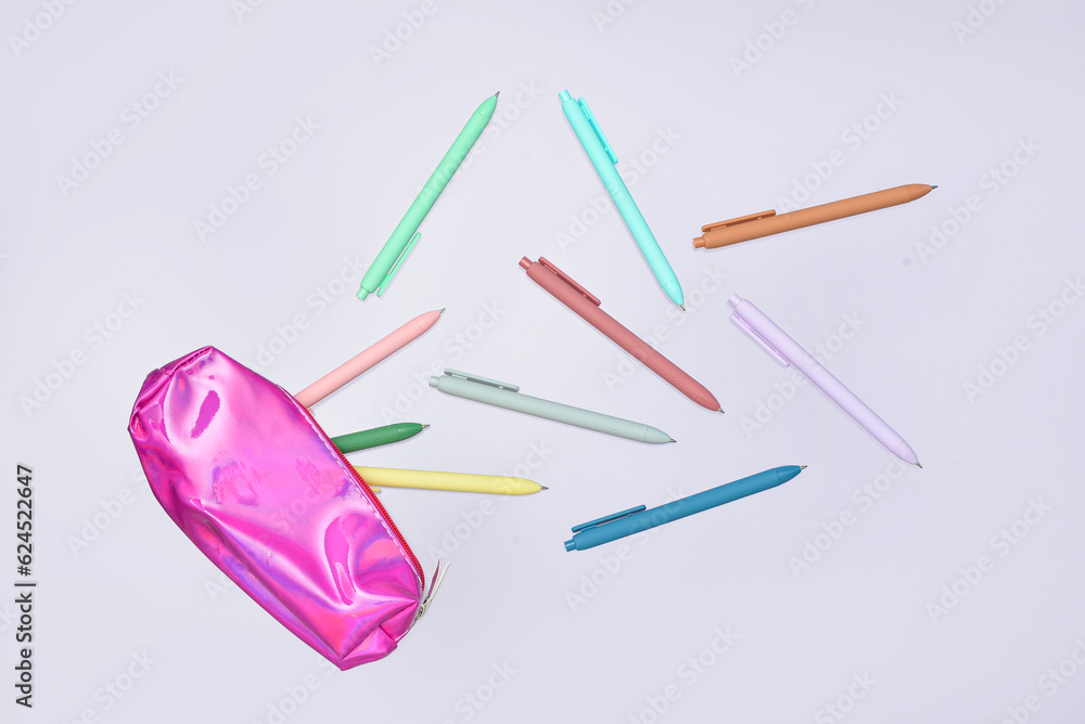 Colorful pens and pink pencil case on lilac background