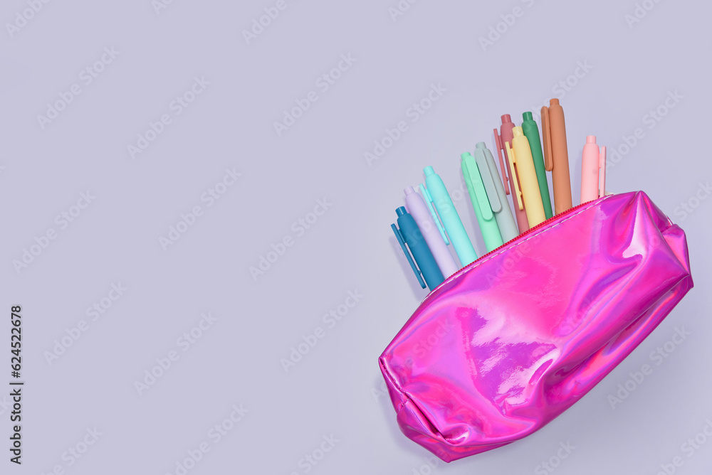 Colorful pens in pink pencil case on lilac background